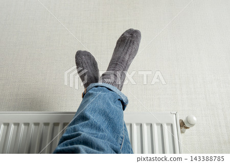 Heating season. Person relaxes at home with feet on heated radiator. Heating season concept 143388785
