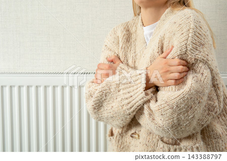 Heating season. Woman embraces herself to stay warm beside radiator. Heating season comfort concept Heating season. Woman embraces herself to stay warm beside radiator. Heating season comfort concept 143388797