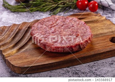 Raw beef patty on wooden cutting board with rosemary and cherry tomatoes Raw beef patty on wooden cutting board with rosemary and cherry tomatoes 143388917