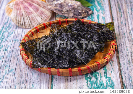 Dried nori seaweed sheets on round woven bamboo tray with red bindings and scallop shell on distressed teal wood surface Dried nori seaweed sheets on round woven bamboo tray with red bindings and scallop shell on distressed teal wood surface 143389028