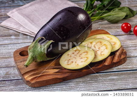 Fresh raw purple eggplant with sliced rounds and spinach leaves on wooden cutting board, healthy vegetable ingredient Fresh raw purple eggplant with sliced rounds and spinach leaves on wooden cutting board, healthy vegetable ingredient 143389031