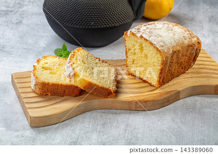 Wooden cutting board with sliced pound cake dusted with powdered sugar, fresh mint garnish, and whole lemon in background, baked dessert Wooden cutting board with sliced pound cake dusted with powdered sugar, fresh mint garnish, and whole lemon in background, baked dessert 143389060