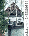 closeup of rustic wooden house with green roof and stone fence in snowy winter forest, birch trees and wooden railing, countryside lifestyle, tourism and seasonal recreation, vertical 143389644