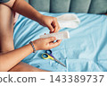 Close-up of a woman hand preparing a sterile gauze bandage for dressing an injured leg at home. Medical supplies and scissors are visible, illustrating first aid, wound care, home treatment 143389737