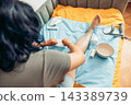 Woman changing a bandage on her injured leg while recovering at home. Medical supplies, crutch, and home care equipment are visible, illustrating first aid, rehabilitation, wound treatment, and 143389739