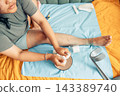 plus size young woman performing home wound care for a bruised and injured leg while sitting on a bed with gauze pads, bandages, and a crutch nearby, illustrating recovery, first aid, and 143389740