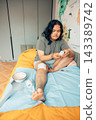 plus size young woman sitting on bed and applying a gauze bandage to her injured leg at home. visible scars and bruising on the knee and thigh. home first aid, wound care, injury recovery 143389742