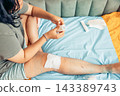 plus size young woman sitting on bed and applying a gauze bandage to her injured leg at home. visible scars and bruising on the knee and thigh. home first aid, wound care, injury recovery 143389743