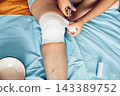 person cutting medical bandage from leg after surgery, home wound care on bed with blue sheet, yellow blanket, recovery process, healthcare, medical service, rehabilitation, top view 143389752