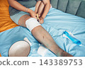 person cutting medical bandage from leg after surgery, home wound care on bed with blue sheet, yellow blanket, recovery process, healthcare, medical service, rehabilitation 143389753