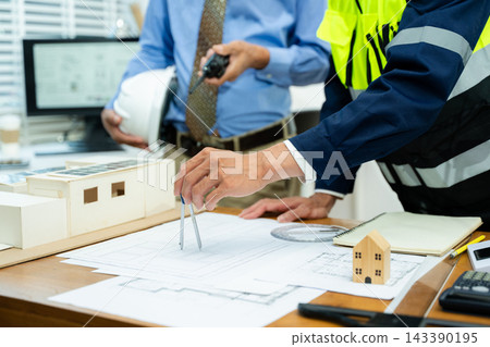Two colleagues discussing data working and tablet, laptop with on on architectural project at construction site at desk Two colleagues discussing data working and tablet, laptop with on on architectural project at construction site at desk 143390195