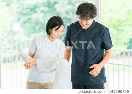 一名年輕的女員工正在接受按摩和物理治療培訓，一名男性物理治療師正在指導她。 143390709