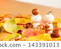 A peg doll surrounded by fallen autumn leaves, with an acorn on its head. 143391013