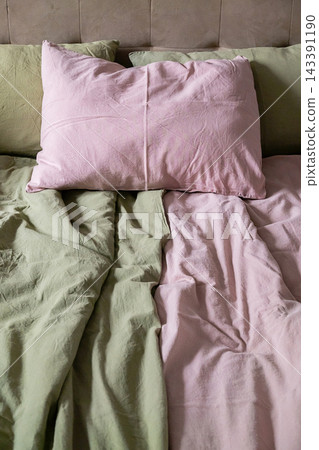 Unmade Bed with Soft Pastel Green and Pink Linen Bedding in Cozy Bedroom Interior Unmade Bed with Soft Pastel Green and Pink Linen Bedding in Cozy Bedroom Interior 143391190
