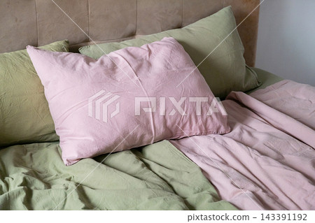 Unmade Bed with Soft Pink and Olive Green Linen Bedding and Pillows in Cozy Home Interior Unmade Bed with Soft Pink and Olive Green Linen Bedding and Pillows in Cozy Home Interior 143391192