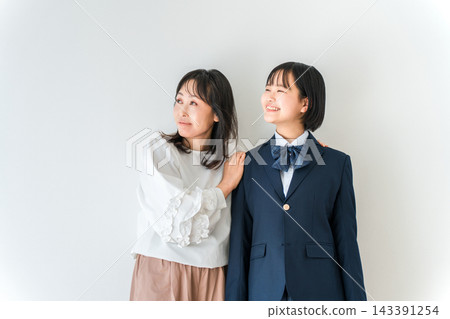 一位母親面帶微笑,站在身穿校服的高中女兒身邊。母女倆抬頭望著彼此。 一位母親面帶微笑,站在身穿校服的高中女兒身邊。母女倆抬頭望著彼此。 143391254