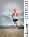 Athletic bearded man running on a mountain road wearing trail running gear against a scenic alpine landscape background Athletic bearded man running on a mountain road wearing trail running gear against a scenic alpine landscape background 143391488
