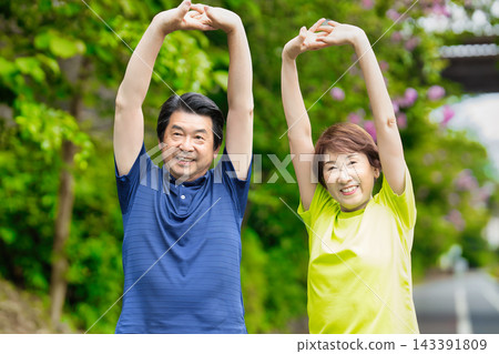 一對老年夫婦在綠樹叢中伸展身體,露出笑容。 一對老年夫婦在綠樹叢中伸展身體,露出笑容。 143391809
