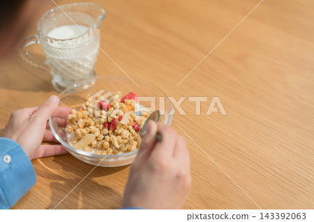 A woman's hands scooping granola with a spoon. A woman's hands scooping granola with a spoon. 143392063