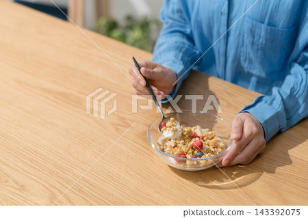 一位女士用湯匙舀格蘭諾拉麥片。 一位女士用湯匙舀格蘭諾拉麥片。 143392075