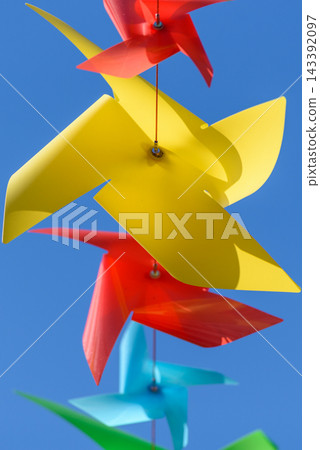 A close-up view showcasing a vertical arrangement of colorful plastic windmill-shaped pinwheels against a clear blue sky A close-up view showcasing a vertical arrangement of colorful plastic windmill-shaped pinwheels against a clear blue sky 143392097