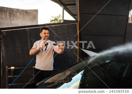 Happy man washing car with pressure washer outdoors Happy man washing car with pressure washer outdoors 143393539