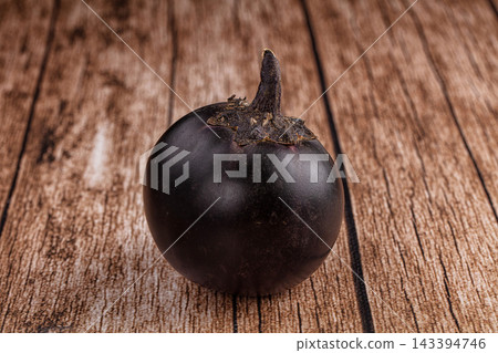 Rustic wooden tabletop supporting single round purple eggplant with stem, organic vegetable ingredient Rustic wooden tabletop supporting single round purple eggplant with stem, organic vegetable ingredient 143394746