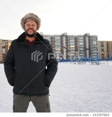 Front view of an angry aggressive bearded man growling on snow outdoors wearing warm winter fur hat. 143397603