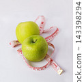 Two fresh green apples with a measuring tape on a clean white surface, representing healthy eating, weight management, nutrition, fitness, and wellness lifestyle concepts 143398294