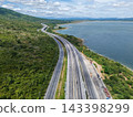 Drone aerial view of a highway running beside a reservoir with lush green mountains, Transportation infrastructure and renewable energy concept 143398299