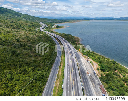 Drone aerial view of a highway running beside a reservoir with lush green mountains, Transportation infrastructure and renewable energy concept Drone aerial view of a highway running beside a reservoir with lush green mountains, Transportation infrastructure and renewable energy concept 143398299