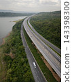 Drone aerial view of an elevated highway crossing lush forest and mountain landscape under dramatic clouds, The modern transportation infrastructure and nature concept 143398300