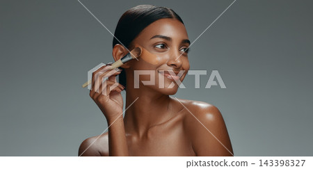 Beauty, makeup and foundation brush of a woman with cosmetics, smile and dermatology. Portrait of a happy Indian model person with facial care, skin glow and wellness on a grey background in studio Beauty, makeup and foundation brush of a woman with cosmetics, smile and dermatology. Portrait of a happy Indian model person with facial care, skin glow and wellness on a grey background in studio 143398327