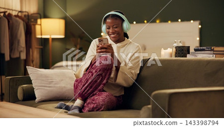 African woman, headphones and phone on sofa with smile, laugh and excited for music in home living room. Girl, smartphone and happy for streaming, audio subscription and mobile app on couch in house 143398794