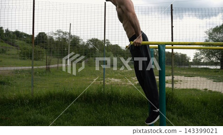Young sportsman doing push ups on parallel bars at nature. Strong sporty man exercising at sports ground. Male shirtless athlete training hard outdoor. Concept of active sportive lifestyle. Slow mo Young sportsman doing push ups on parallel bars at nature. Strong sporty man exercising at sports ground. Male shirtless athlete training hard outdoor. Concept of active sportive lifestyle. Slow mo 143399021