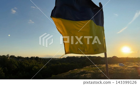 National flag of Ukraine waving on hilltop against a bright golden sunset. View of Ukrainian banner fluttering in the wind, symbolizing the fight for independence, resilience and freedom National flag of Ukraine waving on hilltop against a bright golden sunset. View of Ukrainian banner fluttering in the wind, symbolizing the fight for independence, resilience and freedom 143399126