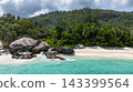 Granite boulders situated by turquoise ocean waters, set against lush forested hills. Seychelles, Mahe. Roche Copra. 143399564
