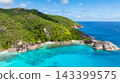 Expansive green hills covered in dense vegetation meet the wide expanse of clear blue ocean with rocky formations. Seychelles, Mahe. 143399575