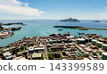Harbor with industrial buildings, storage tanks, containers, and turquoise sea, with green islands in the background. Seychelles, Mahe. Victoria. 143399589