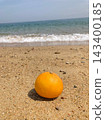 一個孤零零的橘子靜靜地躺在沙灘上,海浪拍打著它。這是夏日的海灘。 一個孤零零的橘子靜靜地躺在沙灘上,海浪拍打著它。這是夏日的海灘。 143400185