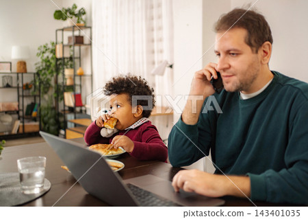 Father working from home with son eating snack Father working from home with son eating snack 143401035