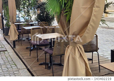Outdoor Urban Cafe Setting with Elegant Drapes and Cozy Seating for Tranquil Dining Outdoor Urban Cafe Setting with Elegant Drapes and Cozy Seating for Tranquil Dining 143402219