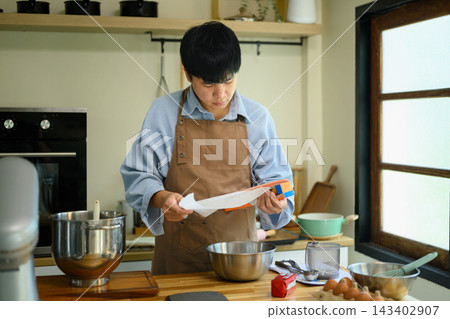 Young Asian Man Preparing Parchment Paper for Cookie Baking in Home Kitchen Young Asian Man Preparing Parchment Paper for Cookie Baking in Home Kitchen 143402907