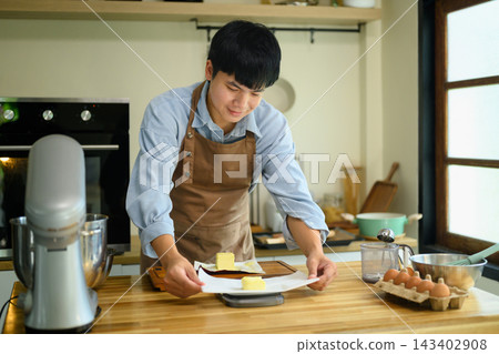 Young Asian Man Measuring Butter on Kitchen Scale for Dessert Baking at Home 143402908