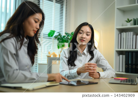 Two Asian Businesswomen Collaborating Over Tablet in Modern Office Workspace 143402909