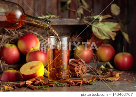 Apple juice on an old kitchen table next to fresh apples, cinnamon, anise, and rosemary. Apple juice on an old kitchen table next to fresh apples, cinnamon, anise, and rosemary. 143403767