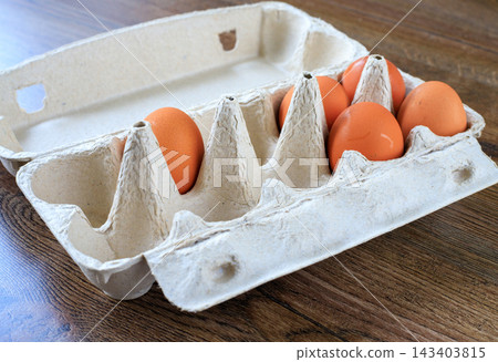 Brown chicken eggs placed in an open eco-friendly paper carton package resting on a wood background. Sustainable food packaging 143403815