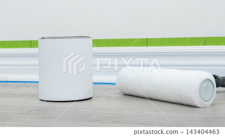 Home renovation mockup featuring a paint can and roller on wooden flooring with painter's tape and wall preparation visible Home renovation mockup featuring a paint can and roller on wooden flooring with painter's tape and wall preparation visible 143404463