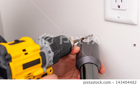 Mans hands holding yellow cordless drill with bit near wall outlet, ready for drilling. Home improvement, preparing to drill, DIY drilling, tool handling. Mans hands holding yellow cordless drill with bit near wall outlet, ready for drilling. Home improvement, preparing to drill, DIY drilling, tool handling. 143404482