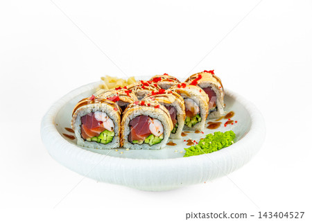 Sushi roll with tuna, salmon, shrimp and cucumber topped with baked spicy sauce, red tobiko and unagi sauce on white plate, white background Sushi roll with tuna, salmon, shrimp and cucumber topped with baked spicy sauce, red tobiko and unagi sauce on white plate, white background 143404527